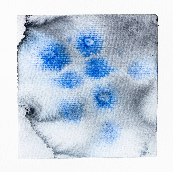 Beispiel der Aquarellmalerei von Hand in grauer Farbe auf texturiertem weißem Papier in Nahaufnahme gezeichnet - Flecken in blauen Aquarelltropfen auf nass bemalter grauer Oberfläche - Foto, Bild