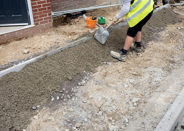 Groundworker colocação e nivelamento com a pá um concreto semi-seco em torno de afiação kerb durante a construção do caminho em frente a nova casa de construção - Foto, Imagem