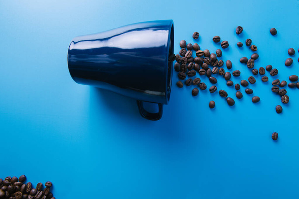 top view of coffee beans poured from a cup on a blue background - 写真・画像