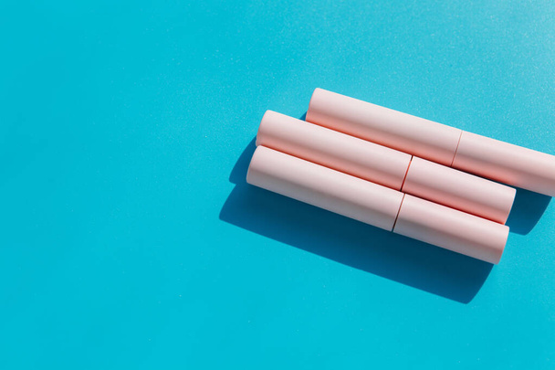pink tubes of cosmetics on a blue background. Copy space. Closed tubes of lipstick, liquid lip gloss, mascara, eyeliner - Foto, Imagem