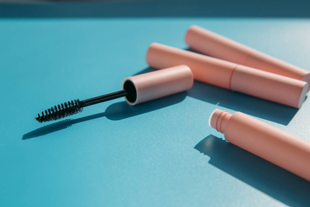 vaaleanpunainen puhdistus meikki harja ripsiväri sijaitsee vieressä avoin putki, suljettu putket kosmetiikka, huulikiilto, nestemäinen huulipuna, vaaleanpunainen rajauskynä sinisellä pohjalla varjoilla. Kopioi tila - Valokuva, kuva