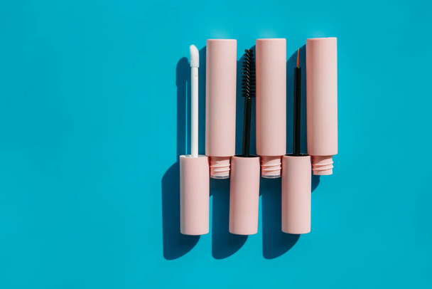 pink tubes of cosmetics and brushes lie on a blue background. Copy space. Closed tubes of lipstick, liquid lip gloss, mascara, eyeliner - Foto, immagini