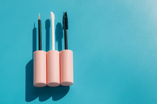 pink brushes for cosmetics, mascara, liquid lipstick, eyeliner, lip gloss on a blue background, copy space - Foto, imagen
