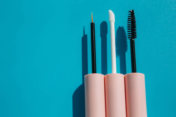 pink brushes for cosmetics, mascara, liquid lipstick, eyeliner, lip gloss on a blue background, copy space - Fotografie, Obrázek