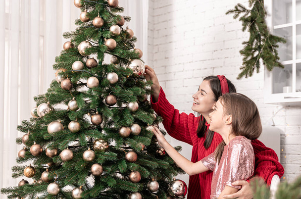 Мама и маленькая дочь украшают елку вместе. - Фото, изображение