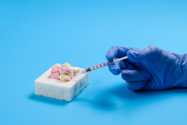 Sweets en een doktershand met een injectiespuit met insuline op een blauwe achtergrond. Diabetes bescherming en behandeling concept. - Foto, afbeelding
