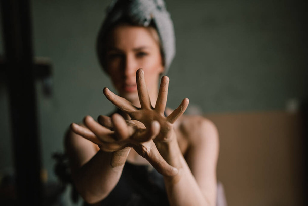 beautiful sculptor girl with a headband and a black apron shows her hands stained with clay. focus of camera is on girl's fingers. concept is beauty - Фото, зображення