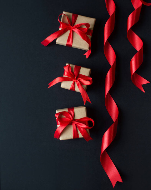 Ünnepi koncepció - ajándékok kézműves papírral, piros íjjal, fekete háttérrel. összetétel karácsonyra, újévre és ünnepekre. lapos fekvés szöveges szöveggel. - Fotó, kép