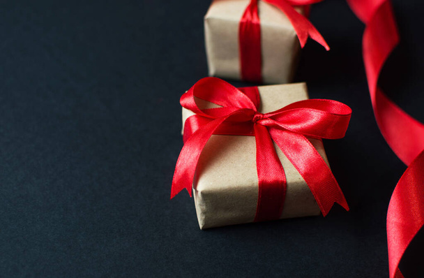 Feestelijke concept - geschenken met ambachtelijk papier met een rode strik op een zwarte achtergrond. samenstelling voor kerst, nieuwjaar en feestdagen. plat lag met plaats voor tekst. - Foto, afbeelding