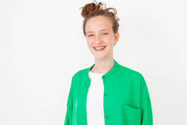 Cut young female girl with happy smile, turn head at camera and looking cheerful, standing against white background in green shirt. Portrait of fun teen student Studio Shot - Zdjęcie, obraz