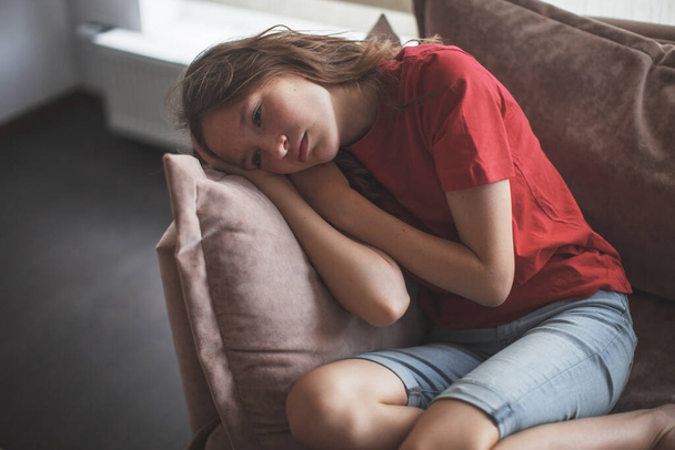 Sad thoughtful teen girl sits on couch feels depressed, offended or lonely, upset young woman suffers from abuse, harassment or heartbreak, grieving lady or violence victim has psychological problem - Foto, Imagen