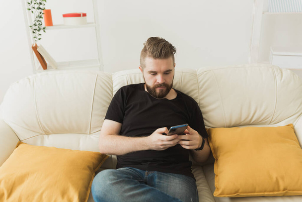 Handsome hipster man using cellphone at home. Communication leisure and technologies concept - Фото, изображение