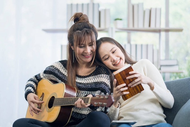 Deux jeunes lesbiennes jouent de la musique. guitare et kalimba sur le canapé dans le salon - Photo, image