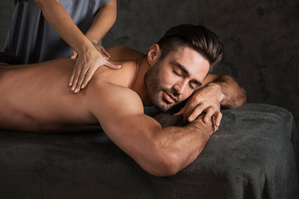 A good-looking man getting a back massage lying down in SPA - Фото, изображение