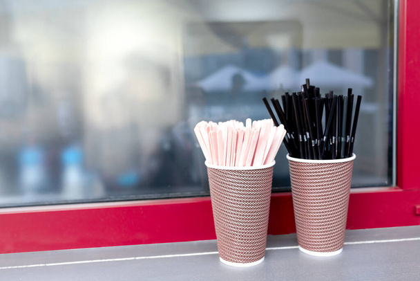 Black cocktail tubes with corrugation, wooden stirring sticks in paper cups in front of a coffee shop window. Copy space - Photo, Image