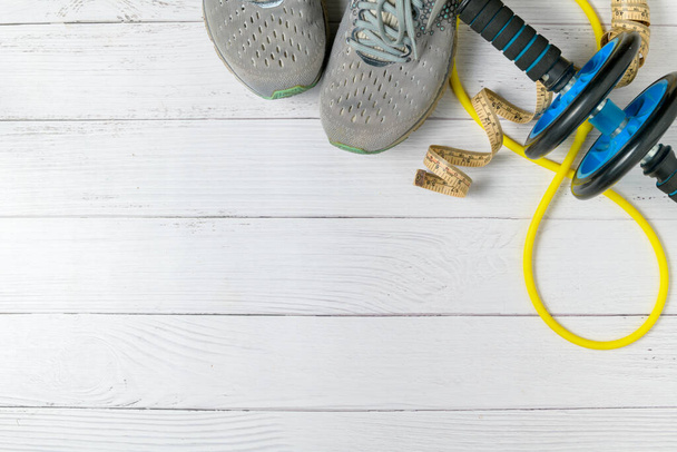 běžecké boty a břišní cvičení a páska v pase na bílém dřevěném pozadí.koncept cvičení pro hubnutí - Fotografie, Obrázek