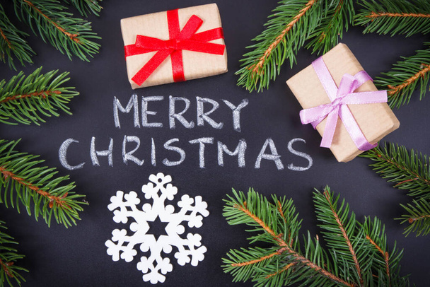 Επιγραφή Καλά Χριστούγεννα, τυλιγμένα δώρα με κορδέλα και πράσινα κλαδιά ερυθρελάτης σε μαύρο φόντο. Διακόσμηση για τα Χριστούγεννα - Φωτογραφία, εικόνα