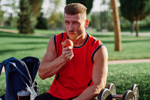 sporty man resting in the park on a bench having a snack - Zdjęcie, obraz