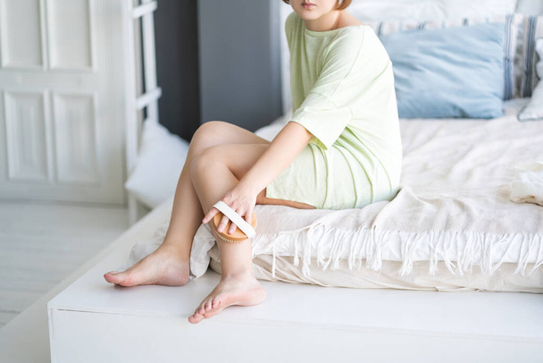 Woman makes a lymphatic drainage massage of the legs with a dry brush, body care concept, home interior - 写真・画像