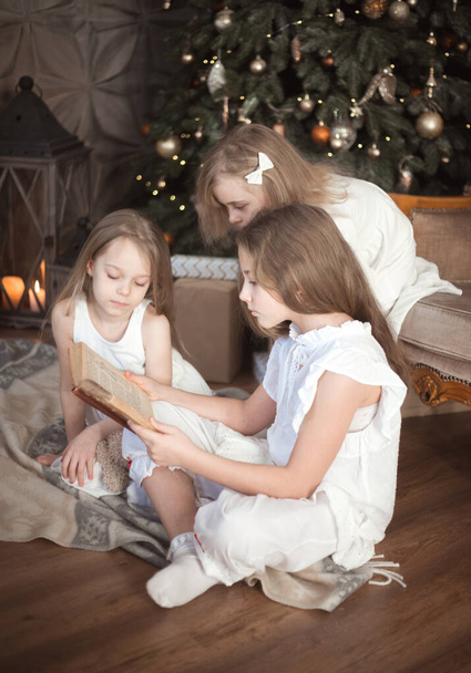 Le sorelle stanno leggendo un libro nella stanza dei bambini. Natale e le vacanze invernali. Foto di alta qualità - Foto, immagini