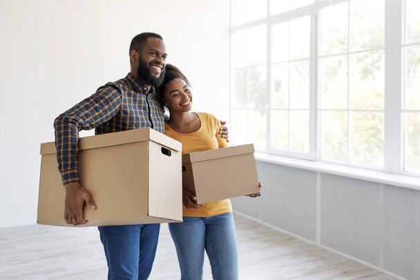 Happy smiling millennial african american couple carry cardboard boxes with belongings, hugging - Photo, Image