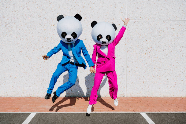 Storytelling image of a couple wearing giant panda head and colored suits. Man and woman making party in a parking lot. - Foto, Bild