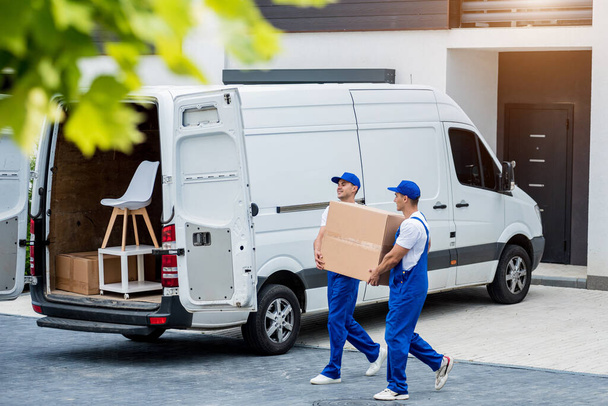 Two removal company workers are loading boxes and furniture into a minibus. - Fotografie, Obrázek