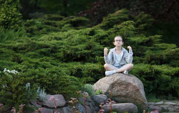 Child girl sitting on the cobblestone in lotus position. Teenage girl practicing yoga. - Photo, Image