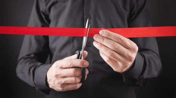 Man cutting red ribbon with a scissors. - 写真・画像