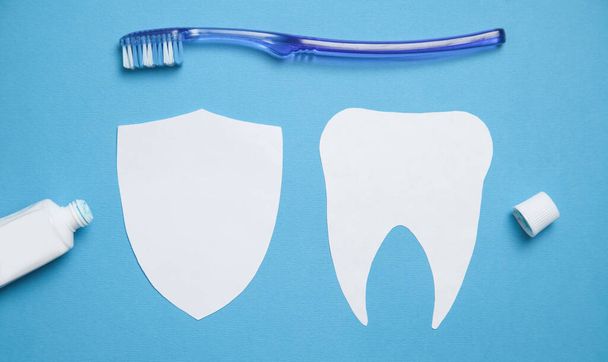 Paper tooth with a toothbrush and toothpaste on blue background. - Photo, Image