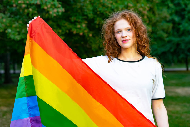 Portrait of young lesbian happy woman, beautiful girl holding rainbow gay flag in LGBT color on summer sunny day on natural background. LGBT community, homosexual equality concept - Foto, Imagen