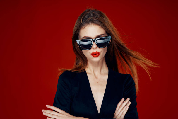 cheerful fashionable woman wearing sunglasses red lips posing red background - Foto, imagen