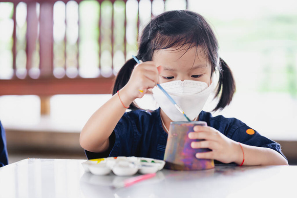 Çocuk fırçayla el işi yapıyor. Virüs ve toz kirliliğini önlemek için cerrahi beyaz yüz maskesi takan küçük kız PM2.5. - Fotoğraf, Görsel