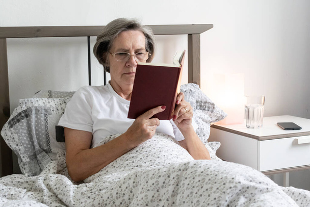 oude veroudering senior vrouw vrouw thuis flat moe ziek alleen gepensioneerd rusten virus ongelukkig verdrietig, lezen boek gelukkig genieten. - Foto, afbeelding