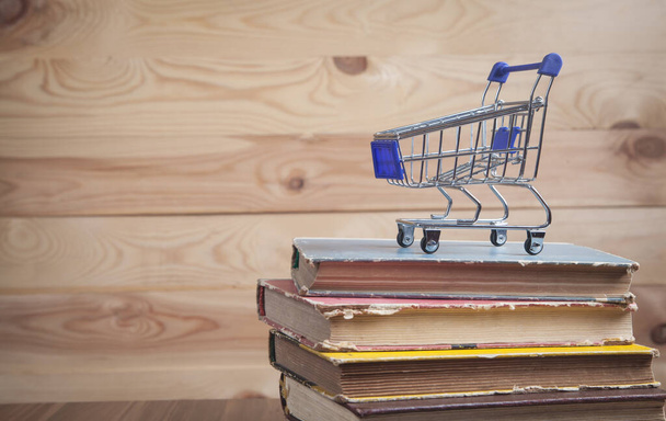 Shopping cart and books on wooden background. - Photo, Image