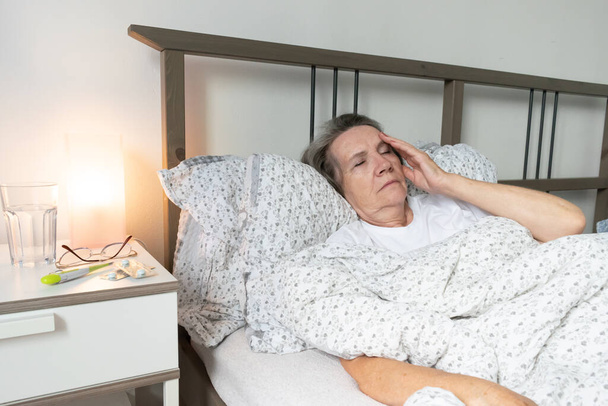 старение пожилая женщина женщина в постели дома, усталый больной один вышел на пенсию и отдых вирус несчастный грустная головная боль мигрень. - Фото, изображение