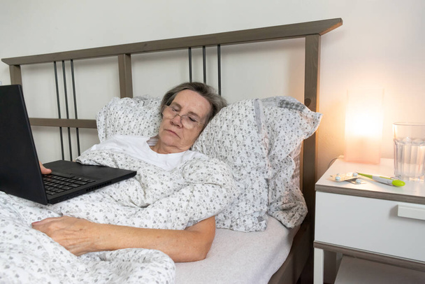 old aging senior woman female in bed flat working home office holding laptop Jobs for Retirees sleeping. - 写真・画像