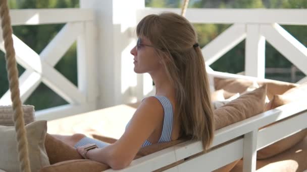 Jonge gelukkige brunette vrouw liggend op een terrasbank met zachte kussens genietend van warme zomerdag. Begrip vrije tijd in de frisse lucht - Video