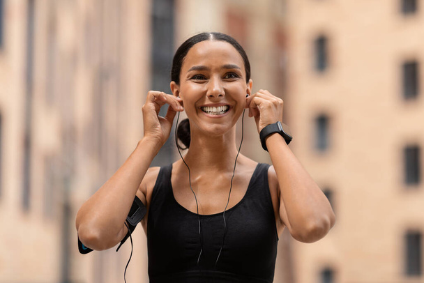 Seznam skladeb na cvičení. Šťastný mladý atletický dáma dávat na sluchátka před jogging venku - Fotografie, Obrázek