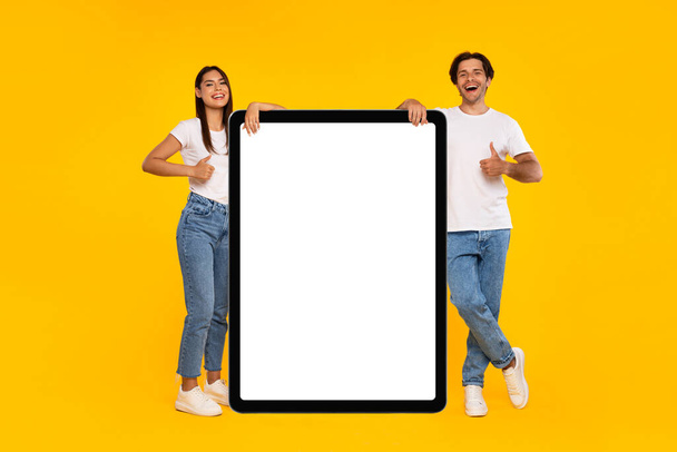 Couple showing white empty tablet screen and gesturing thumbs up - Foto, immagini