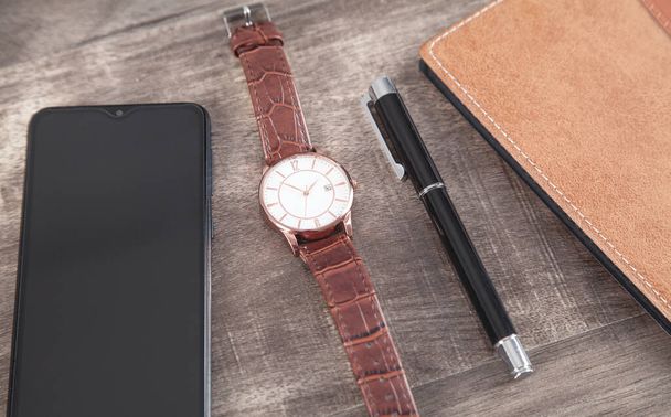Zegarek na rękę, smartfon, długopis, notatnik na drewnianym tle. - Zdjęcie, obraz