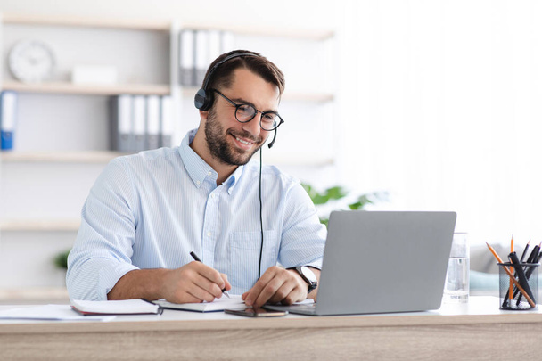 szczęśliwy Dojrzałe biały mężczyzna w okulary i słuchawki praca na laptop w salonie lub w biurze - Zdjęcie, obraz