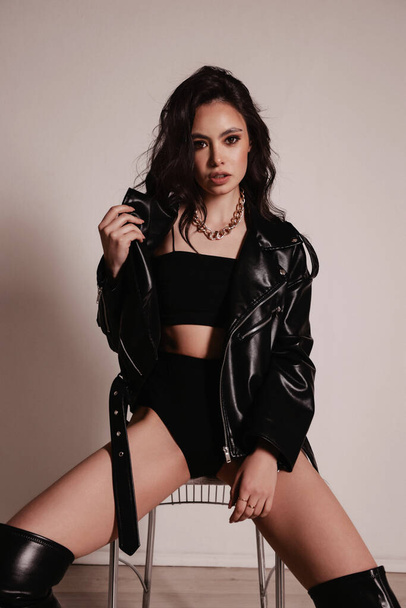 fashion photo of beautiful woman with dark hair in black leather jacket and boots posing in studio - Zdjęcie, obraz