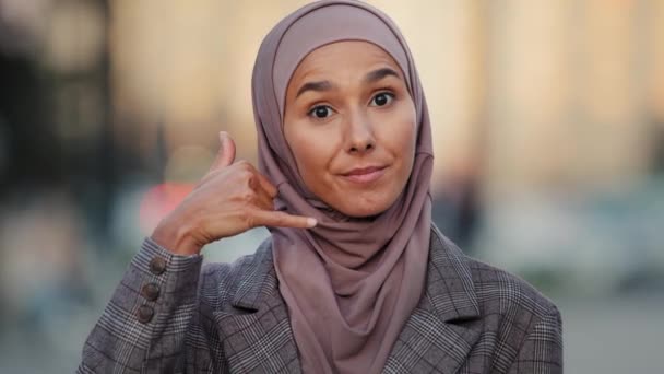 Chiamami. Segnale di chiamata. Ritratto attraente islamica musulmana araba donna d'affari guardando macchina fotografica giocoso flirtare ragazza in città tenendo telefono mano telefono gesto vicino all'orecchio chiedendo offerta di contatto - Filmati, video