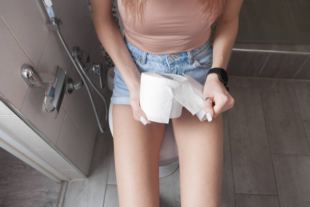 Woman sitting on toilet holding toilet paper. - Valokuva, kuva