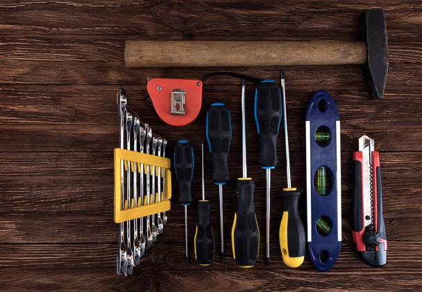 Locksmith's working tool. Mechanical assembly and disassembly tool. Screwdrivers, pliers, wire cutters, building level, tape measure, hammer, wrenches, square and other tools on a wooden surface. - Photo, Image