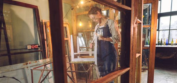 A panorama of woman renovating a chair. Young woman wearing apron working in the workshop. Upcycling concept. - Foto, Bild
