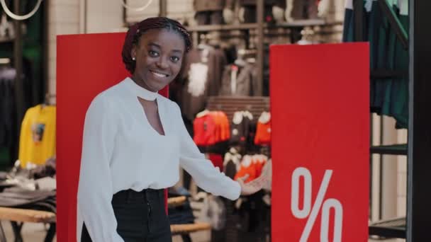 Black Friday concept. Smiling welcoming afro american woman saleswoman african girl consultant boutique store worker standing in shopping mall inviting to buy clothes at big discounts sale low prices - Footage, Video