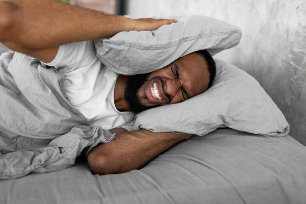 Stressaantunut musta mies peittää korvat makaa sängyssä - Valokuva, kuva