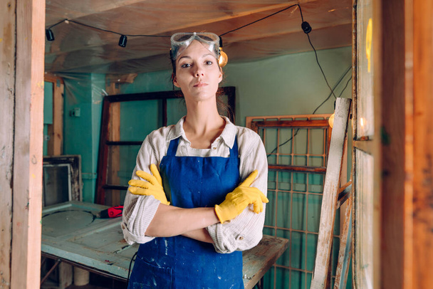 A portrait of a woman wearing protective glasses, gloves and apron working in the workshop. Upcycling concept. - Zdjęcie, obraz